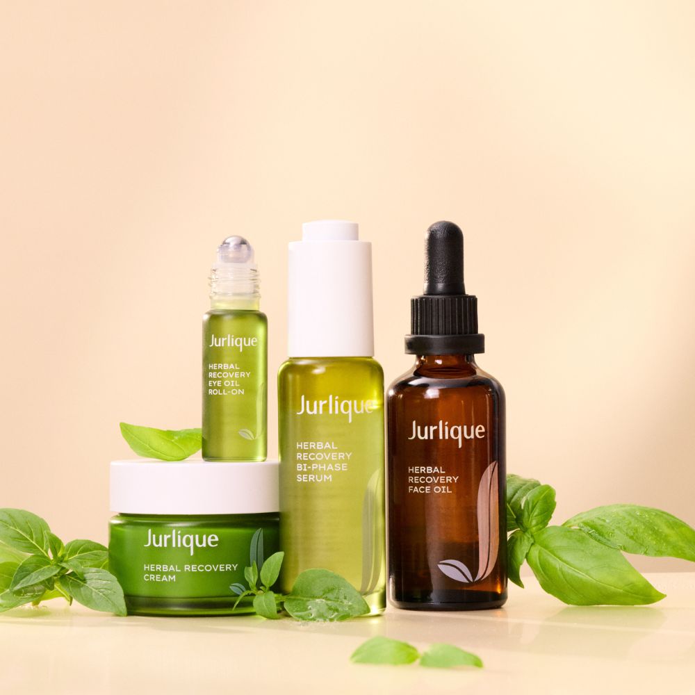 Jurlique skincare products including cream, serum, and face oil on a beige background with green leaves.